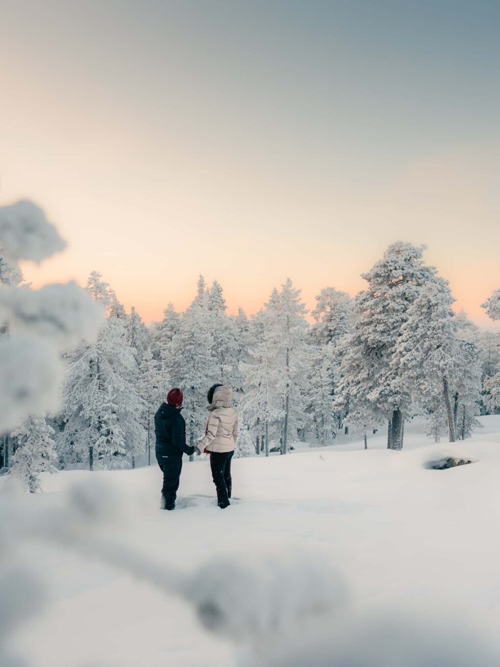 Couple standing in a snowy Lapland landscape at sunset, winter couple photography for tourists